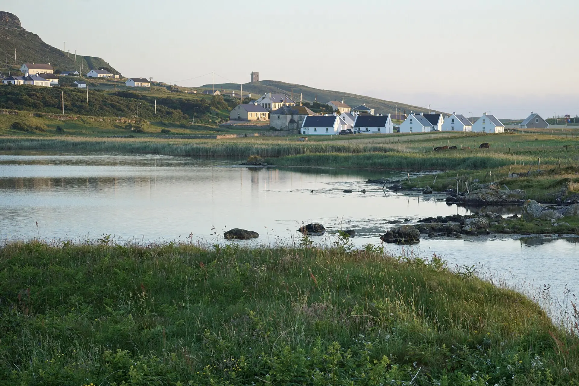 Maghery sna Rosa trasna locha ciúin faoi sholas tráthnóna, le túr Crohy ar an spéirlíne